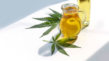 Masadaki kenevir tohumları, cam kavanozdaki yağ, beyaz arka plandaki kenevir yaprakları.