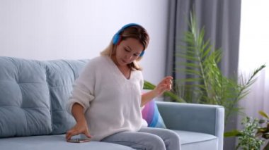 Asyalı güzel bir kadın kulaklık takıyor ve çevrimiçi müzik dinliyor, sosyal medya ve evde podcast sesi. Kız dans ediyor ve evde karantinadayken internette ses ile mutlu..
