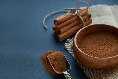 Tarçın çubukları, kenevir ipiyle sade bir şekilde bağlanmış. Ahşap bir kase ve eski bir kepçe içinde yer tarçın. Siyah bir arkaplana yaklaş. metin için boşluk kopyala. Yan görünüm, düz uzanma.