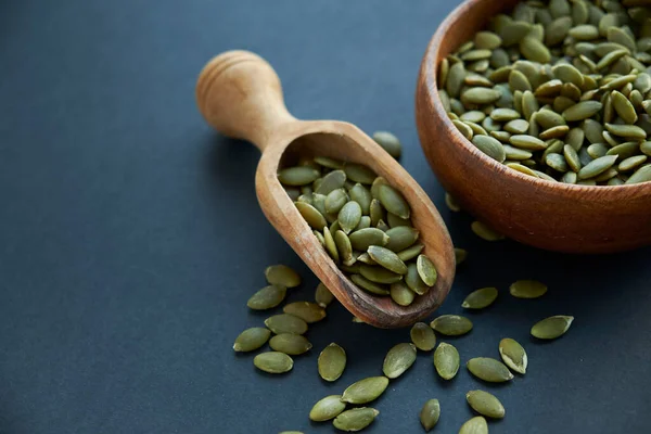Tahta bir kasede kabak çekirdeği ve antika bir kepçe. Siyah bir arkaplana yaklaş. metin için boşluk kopyala