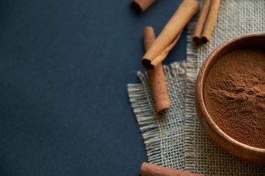 Tarçın çubukları, kenevir ipiyle sade bir şekilde bağlanmış. Ahşap bir kase ve eski bir kepçe içinde yer tarçın. Siyah bir arkaplana yaklaş. metin için boşluk kopyala. Üst manzara, düz uzanma.