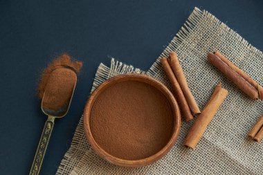 Tarçın çubukları, kenevir ipiyle sade bir şekilde bağlanmış. Ahşap bir kase ve eski bir kepçe içinde yer tarçın. Siyah bir arkaplana yaklaş. metin için boşluk kopyala. Üst manzara, düz uzanma.