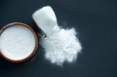 Bir kase kabartma tozu. Bir kaşık bikarbonat. Üst manzara, düz yatış. Siyah bir arkaplana yaklaş. metin için boşluk kopyala.