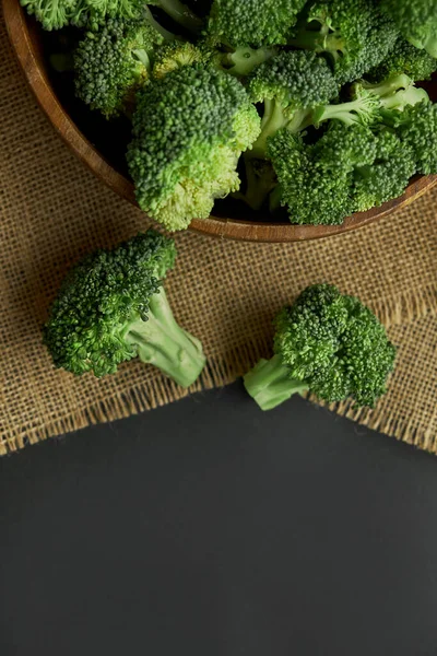 Fresh Broccoli in wooden bowl and seed oil in rustic style. Close up on a black background. copy space for text. Top view, flat lay.