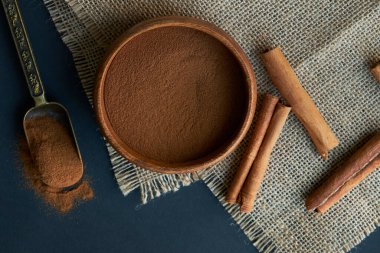 Tarçın çubukları, kenevir ipiyle sade bir şekilde bağlanmış. Ahşap bir kase ve eski bir kepçe içinde yer tarçın. Siyah bir arkaplana yaklaş. metin için boşluk kopyala. Üst manzara, düz uzanma.