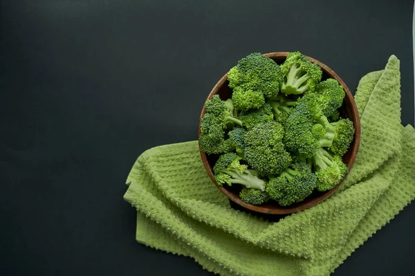 Fresh Broccoli in wooden bowl and seed oil in rustic style. Close up on a black background. copy space for text. Top view, flat lay.