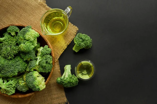 Broccoli freschi in ciotola di legno e olio di semi in stile rustico. Chiudere su uno sfondo nero. copia spazio per il testo. Vista dall'alto, piatta. — Foto Stock