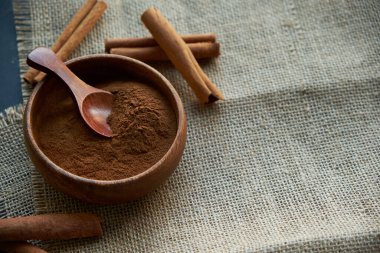 Tarçın çubukları, kenevir ipiyle sade bir şekilde bağlanmış. Ahşap bir kase ve eski bir kepçe içinde yer tarçın. Siyah bir arkaplana yaklaş. metin için boşluk kopyala. Yan görünüm, düz uzanma.