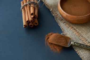 Tarçın çubukları, kenevir ipiyle sade bir şekilde bağlanmış. Ahşap bir kase ve eski bir kepçe içinde yer tarçın. Siyah bir arkaplana yaklaş. metin için boşluk kopyala. Yan görünüm, düz uzanma.