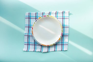 Mavi arka planda beyaz boş bir tabak, sabah güneşinin ışınlarıyla kaplı.