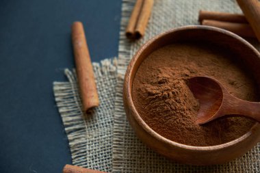 Tarçın çubukları, kenevir ipiyle sade bir şekilde bağlanmış. Ahşap bir kase ve eski bir kepçe içinde yer tarçın. Siyah bir arkaplana yaklaş. metin için boşluk kopyala. Üst manzara, düz uzanma.