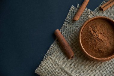 Tarçın çubukları, kenevir ipiyle sade bir şekilde bağlanmış. Ahşap bir kase ve eski bir kepçe içinde yer tarçın. Siyah bir arkaplana yaklaş. metin için boşluk kopyala. Üst manzara, düz uzanma.