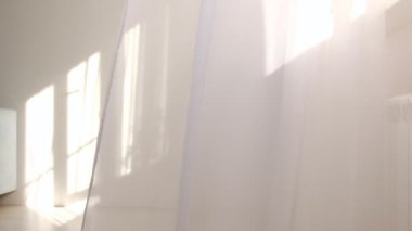 Odadaki açık pencereden rüzgar esiyor. Pencerenin yanında beyaz tül sallıyordu. Sabah güneşi odayı aydınlatıyor, arka plan gölgeli..