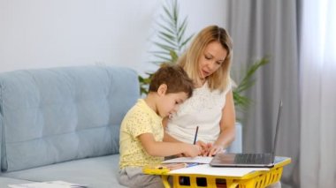 Genç bir anne ya da dadı, küçük bir çocuğun online bir okulda ödevini tamamlamasına yardım eder. Anne ve oğul birlikte okul ödevi yapıyorlar.