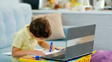 Sanal sınıftaki küçük çocuk. Evde okul var. Küçük şirin çocuk çevrimiçi resim dersi alıyor. Çocuk evde yaratıcılıkla meşgul.