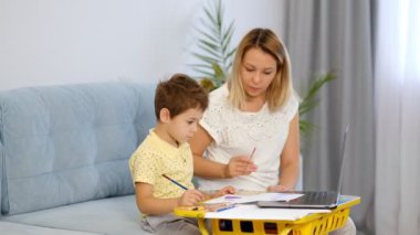 Genç bir anne ya da dadı, küçük bir çocuğun online bir okulda ödevini tamamlamasına yardım eder. Anne ve oğul birlikte okul ödevi yapıyorlar.
