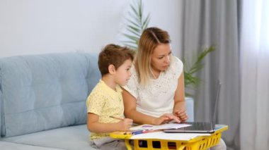 Genç bir anne ya da dadı, küçük bir çocuğun online bir okulda ödevini tamamlamasına yardım eder. Anne ve oğul birlikte okul ödevi yapıyorlar.