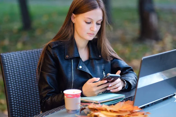 Jovem mulher usando smartphone e laptop fora de um café — Fotografia de Stock