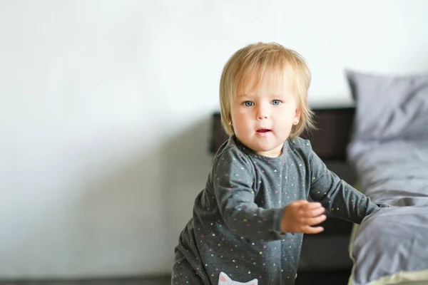 Portrait of very sweet little child. 1 year old baby stands next to the bed. — Stock Photo, Image