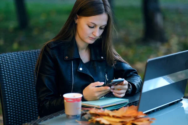 Mulher sorridente navegando na internet. Uma jovem a navegar na Internet no café. jovem mulher usando computador tablet em um café. mulher trabalhando com seu telefone e laptop em um terraço restaurante — Fotografia de Stock