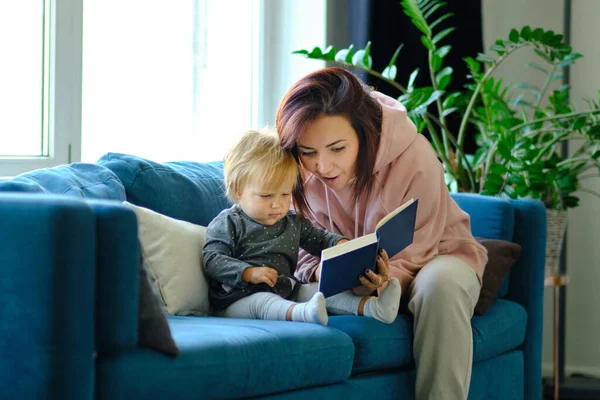 Mother reading a book the baby in sofa. before going to sleep. taking care of children. mothers love for her daughter