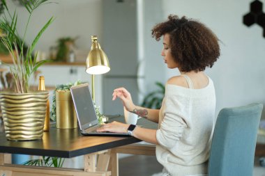 Merkez ofisten çalışan genç bir kadın. Bilgisayarı, telefonu ve interneti kullanan serbest çalışan. Oturma odasındaki işyerinde. Afrikalı Amerikalı kadın blogcu dijital tablet üzerine yeni makalesini yazıyor