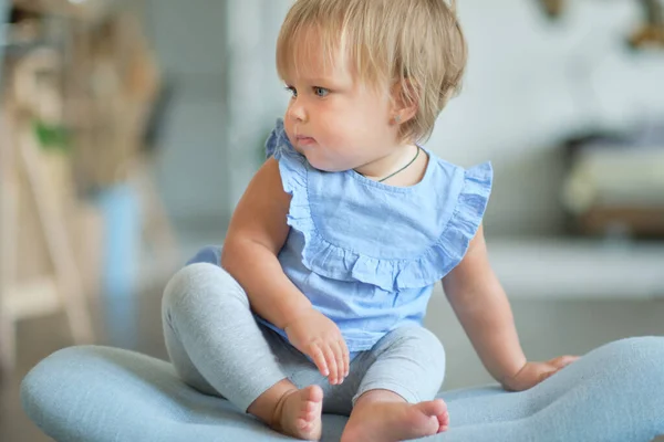 Портрет блондинки с голубыми глазами 1-летней девочки сидит на синем стуле. Симпатичный маленький ребенок играет дома в комнате. — стоковое фото