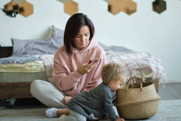 A kislány önállóan játszik a nappaliban, míg anya az interneten — Stock Fotó