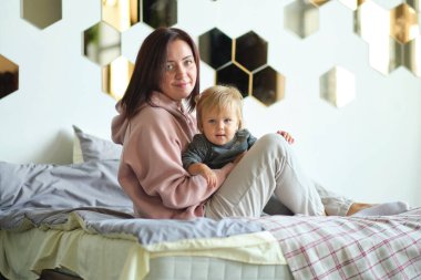 Mutlu aile anne ve bebek oynuyorlar, sarılıyorlar ve yatakta gülüyorlar.