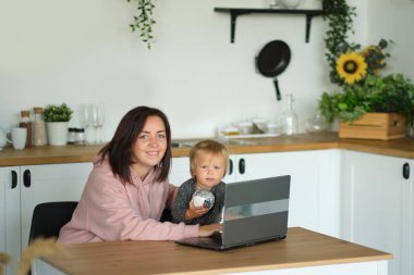 Çocukla birlikte ev ofisinden çalışıyoruz. Ana-kız dizüstü bilgisayar ve internet kullanıyor. Serbest çalışan işyeri. Mutlu kadın küçük çocuğa öğretiyor. Uzaktan öğrenme, izolasyon, evde eğitim. Yaşam tarzı anı