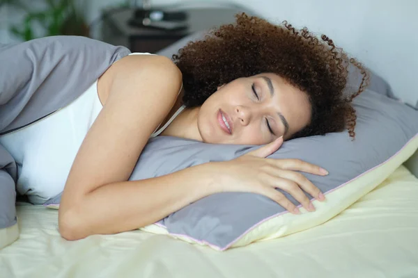 african woman sleeping in her bed at night, she is resting with eyes closed. Cozy bedtime. lady hugging soft white pillow. Lady enjoys fresh soft bedding linen and mattress in bedroom