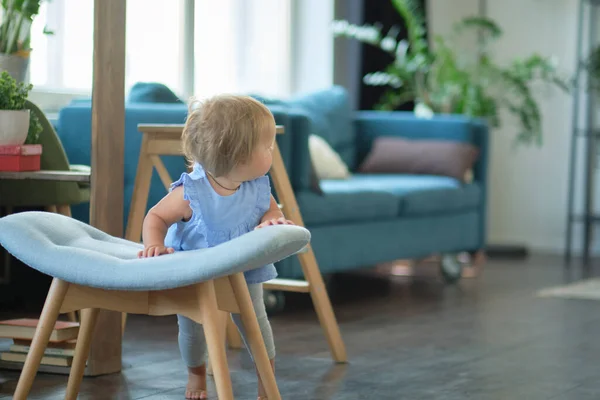 Little blue-eyed girl learns to walk by holding on to the chair. happy baby face — Stock Photo, Image