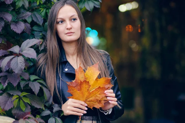 Jonge mooie vrouw in een stijlvolle zwarte leren jas op een achtergrond van wilde druiven. Herfst portret in donkere tinten. dame met esdoorn bladeren — Stockfoto