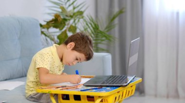 Sanal sınıftaki küçük çocuk. Evde okul var. Küçük şirin çocuk çevrimiçi resim dersi alıyor. Çocuk evde yaratıcılıkla meşgul.