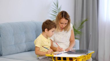 Genç bir anne ya da dadı, küçük bir çocuğun online bir okulda ödevini tamamlamasına yardım eder. Anne ve oğul birlikte okul ödevi yapıyorlar.