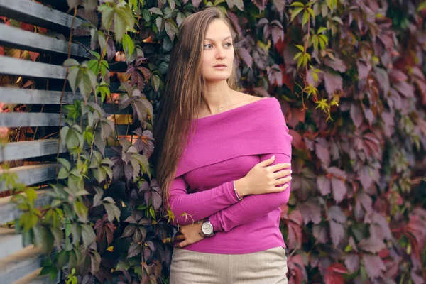 Jeune belle femme dans un pull tricoté rose regarde sur le côté, sur le fond de raisins sauvages. Portrait d'automne. — Photo
