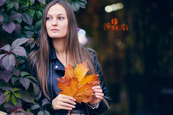 Jovem mulher bonita em uma jaqueta de couro preta elegante em um fundo de uvas selvagens. Retrato de outono em tons escuros. senhora segurando folhas de bordo — Fotografia de Stock