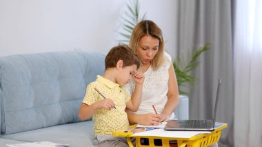 Genç bir anne ya da dadı, küçük bir çocuğun online bir okulda ödevini tamamlamasına yardım eder. Anne ve oğul birlikte okul ödevi yapıyorlar.