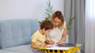 Genç bir anne ya da dadı, küçük bir çocuğun online bir okulda ödevini tamamlamasına yardım eder. Anne ve oğul birlikte okul ödevi yapıyorlar.