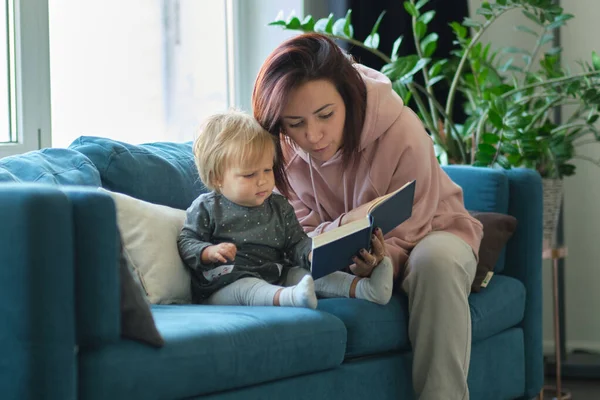 Mother reading a book the baby in sofa. before going to sleep. taking care of children. mothers love for her daughter — Stock Photo, Image