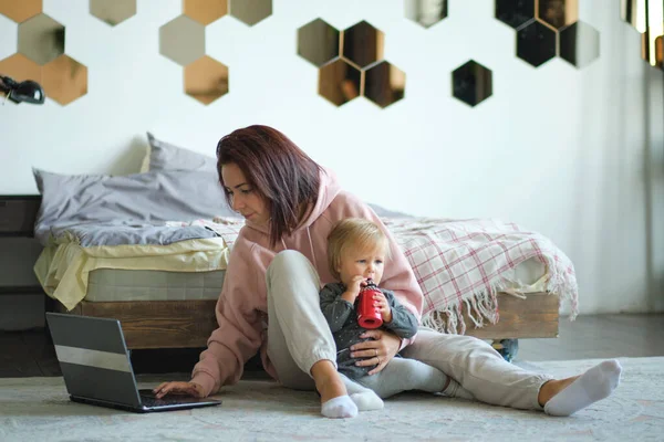 Boldog anya a kislányával, aki laptopot használ otthon a nappaliban. Anya és a baba laptop dolgozik otthonról — Stock Fotó