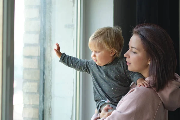 Zblízka krásné maminka objímání dítě v její paži. Mami, podívej se z okna. je šťastná, že je doma s dítětem. — Stock fotografie