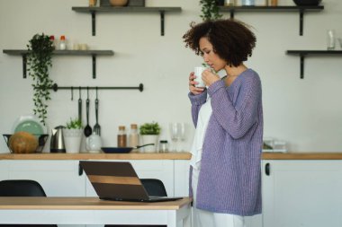 Mutfakta elinde bir fincan kahve tutan mutlu bir kadın. Genç Afro-Amerikan kadın kahve içiyor.