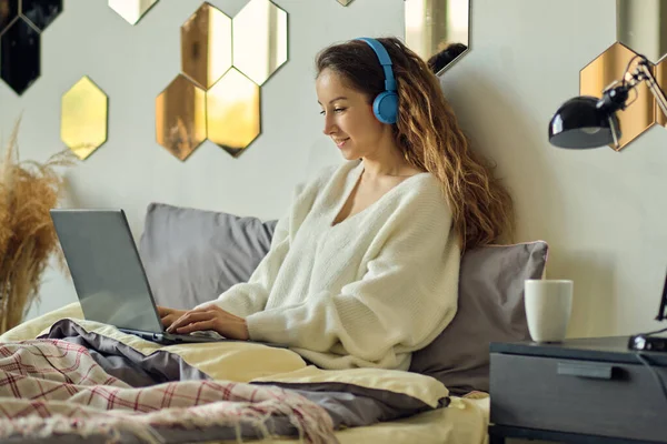 Fiatal gyönyörű nő visel headset használata közben laptop az ágyban — Stock Fotó