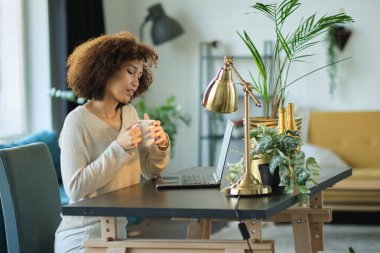 Merkez ofisten çalışan genç bir kadın. Bilgisayarı, telefonu ve interneti kullanan serbest çalışan. Oturma odasındaki işyerinde. Afrikalı Amerikalı kadın blogcu dijital tablet üzerine yeni makalesini yazıyor