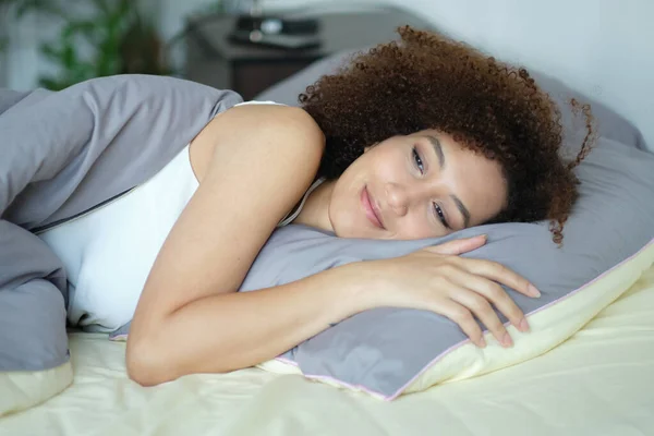 Afrykanka śpi w nocy w łóżku, odpoczywa z zamkniętymi oczami. Przytulna pora spać. Pani przytula miękką białą poduszkę. Lady cieszy się świeże miękkie pościel i materac w sypialni — Zdjęcie stockowe
