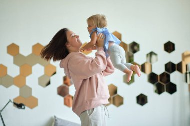 Genç anne çocuğunu kucağında tutuyor. Mutlu ve sevgi dolu bir aile. Anne yatak odasında bebeğiyle oynuyor. Anne gülen çocukla oynuyor. Aile evde.