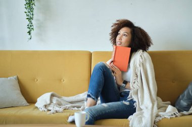 Güzel, Afro-Amerikan bir kadın kitap okuyor. Oturma odasındaki kanepede sırtüstü rahatça yatıyor. Kot pantolonuyla.