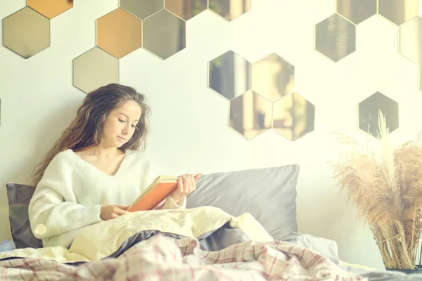Mooie jonge vrouw in een warme gebreide trui leest een boek. lui weekend op een winterochtend. — Stockfoto