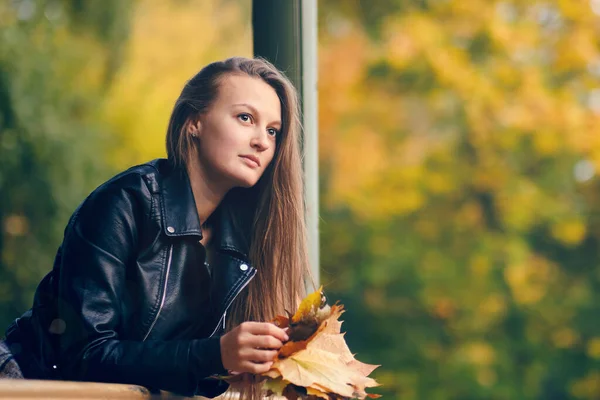 Piękna kobieta patrzy na odległość opierając się o poręcz. portret damy z liśćmi klonu w rękach — Zdjęcie stockowe